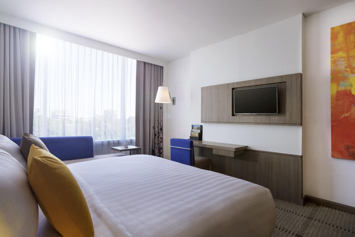 A hotel room with a large bed, a desk, a television, and a window with curtains.