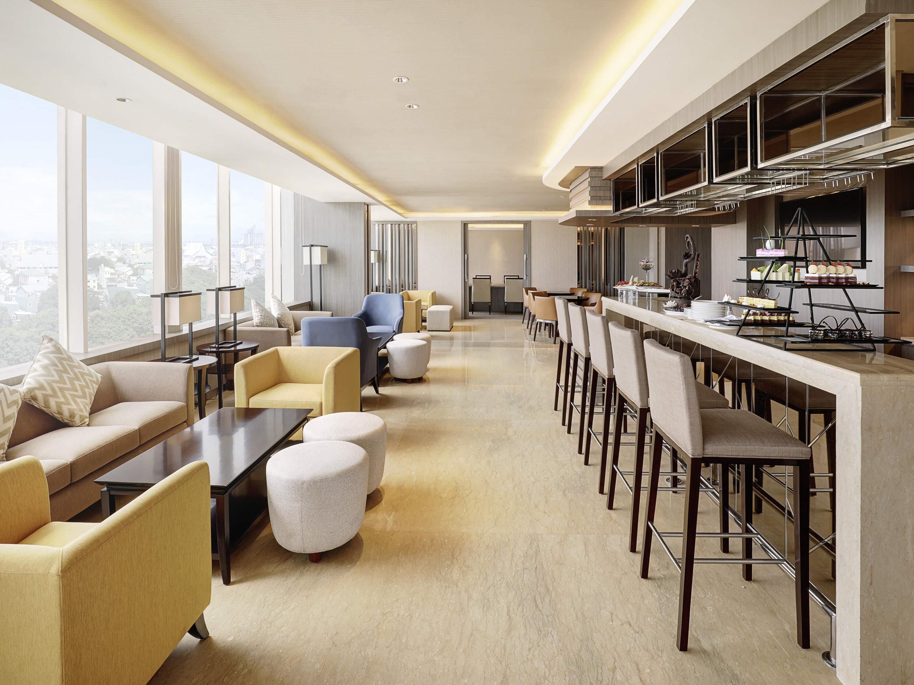 Un hall d’hôtel moderne doté d’un grand espace de restauration, de sièges confortables et d’un comptoir de cuisine où sont présentés des desserts.