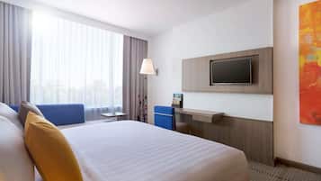 Habitación de hotel con una cama grande, un escritorio, un televisor montado en la pared y una ventana con cortinas.