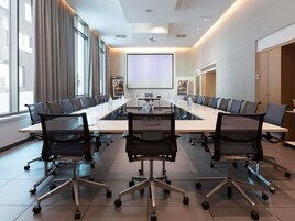 Una sala conferenze con un lungo tavolo, sedie, uno schermo per proiettore e una grande finestra.