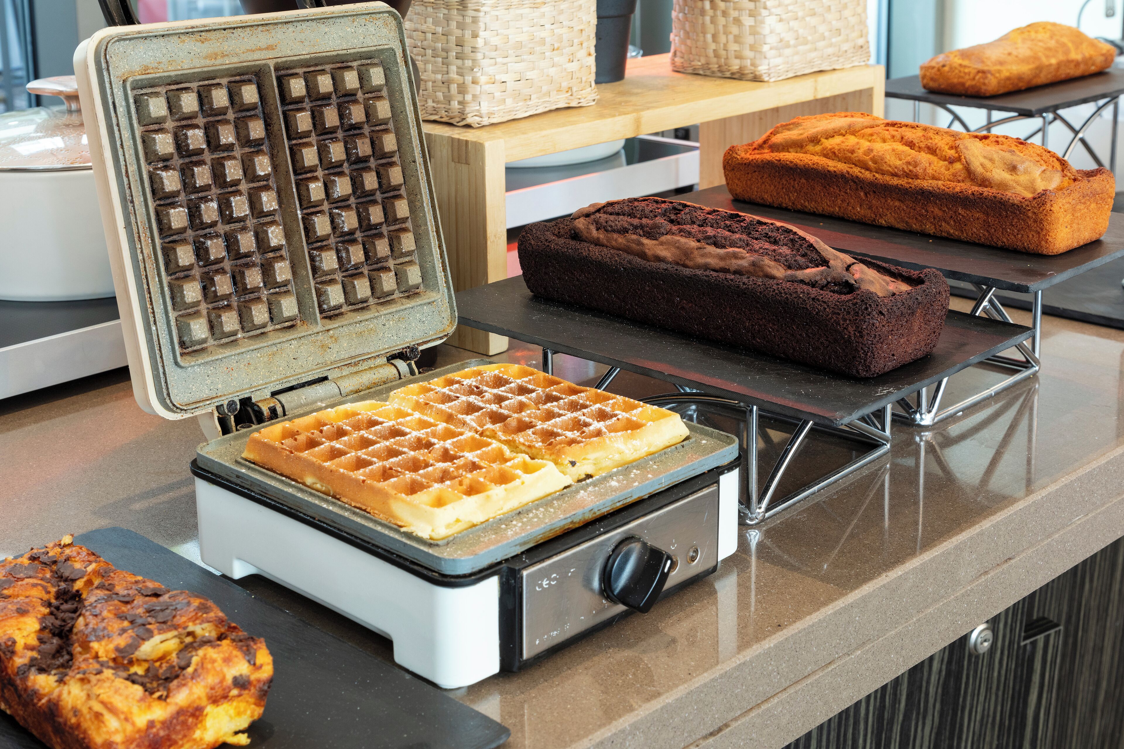 A waffle iron with waffles and a loaf of bread on a kitchen counter.