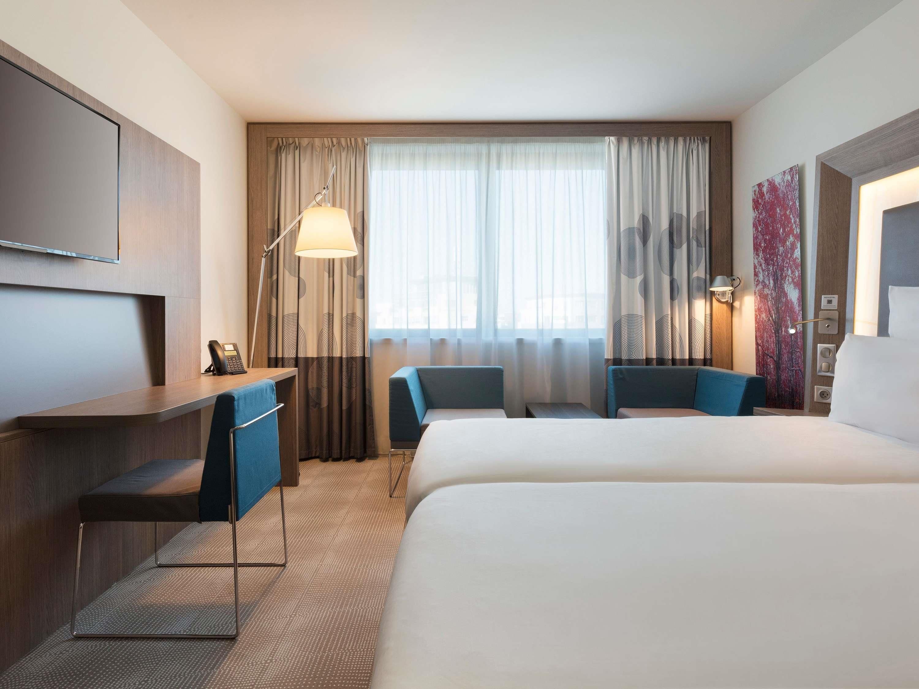 Een hotelkamer met een bed, een bureau, twee stoelen, een televisie en een raam met gordijnen.