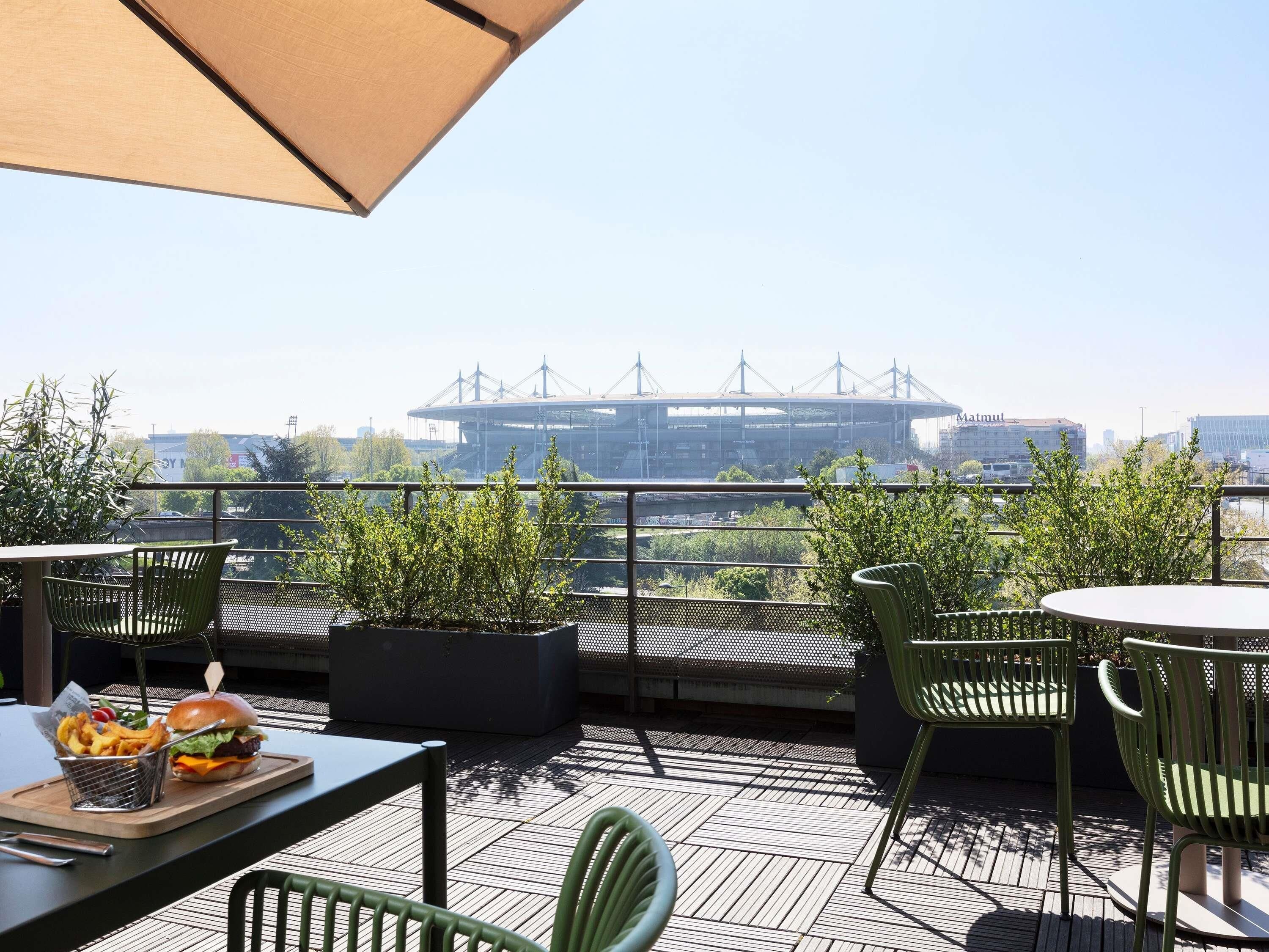 A rooftop terrace with outdoor seating, a view of a bridge, and a burger with fries.