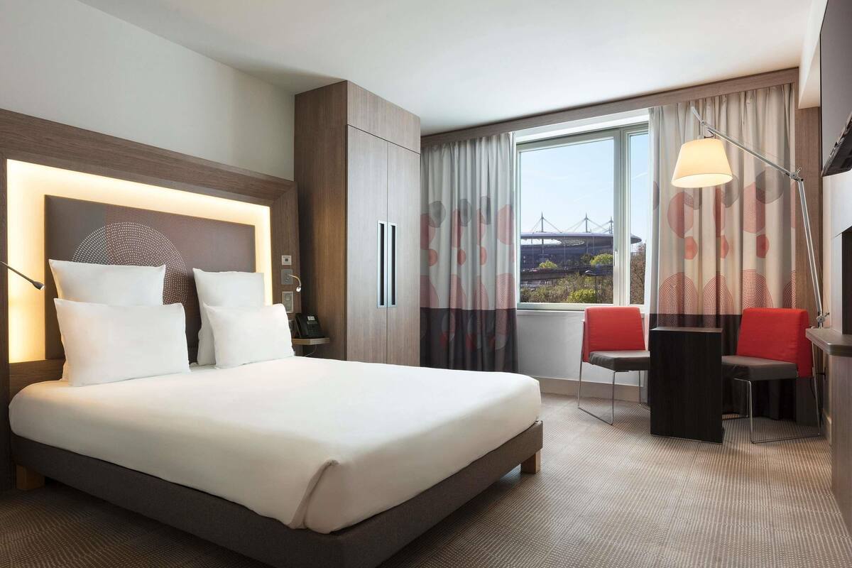 Habitación de hotel con una cama grande, un escritorio con silla, televisión y vistas a un puente.
