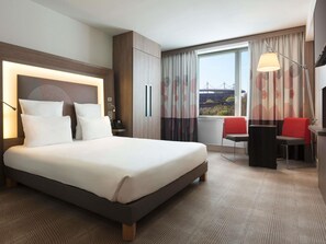 Quarto de hotel com uma cama grande, uma escrivaninha com cadeira, uma televisão e vista para uma ponte.