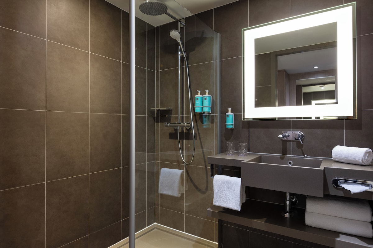 A modern bathroom with a glass-enclosed shower, a large mirror, and a vanity with a sink and towel rack.