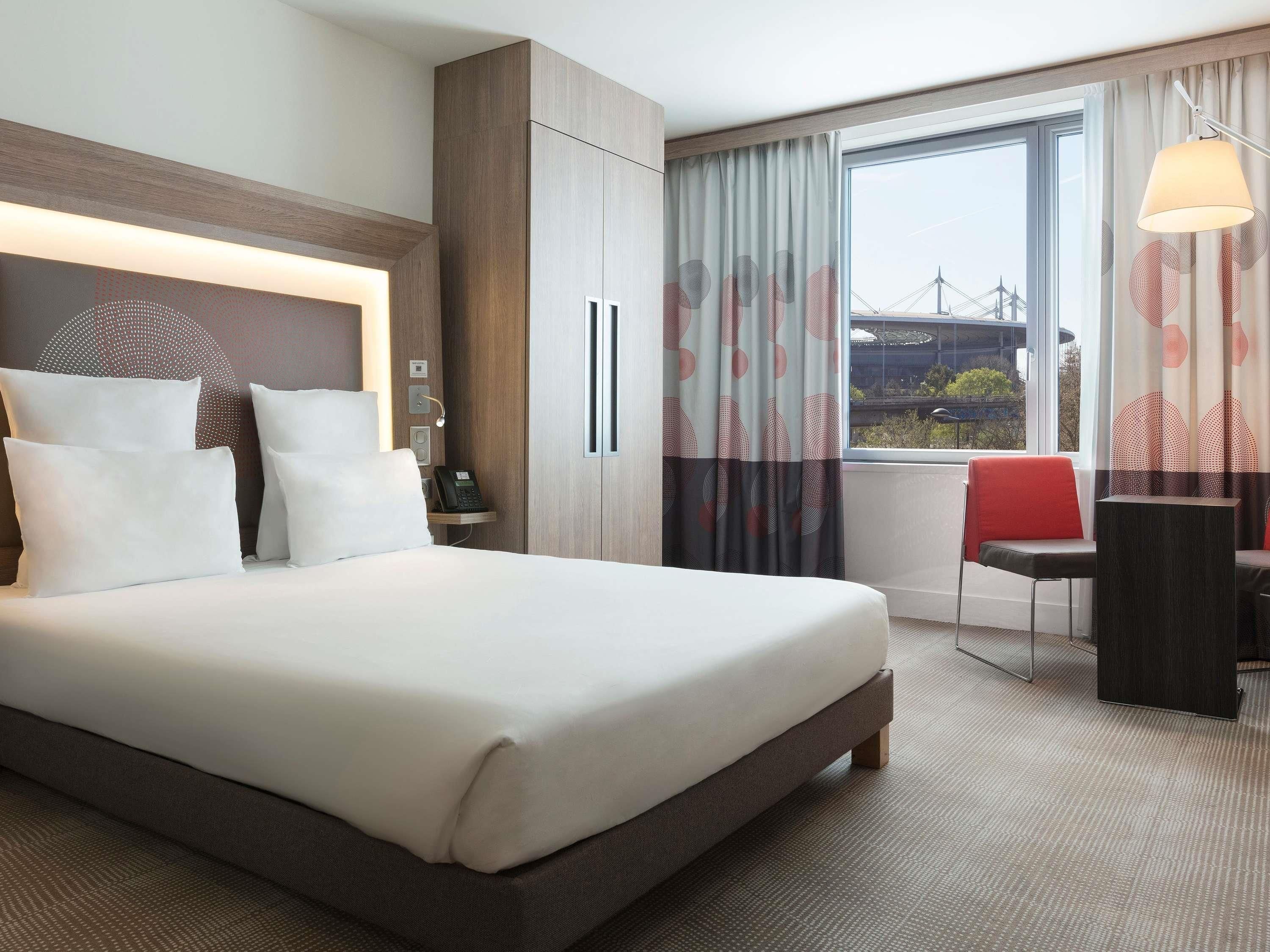 A hotel room with a large bed, a desk, a chair, a lamp, and a window with curtains.