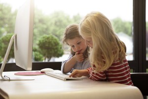 Two individuals at a table with a computer, a keyboard, and a mouse.