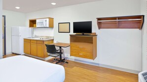 A compact room with a bed, kitchenette, desk, and TV.