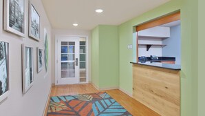 A hallway with a patterned rug, framed pictures on the wall, and a wooden counter with a phone.