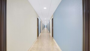 A long, narrow hallway with doors on both sides, leading to rooms. The floor is tiled, and the walls are painted in light and dark blue.