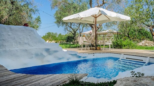 A swimming pool with a wooden deck, a white umbrella, and outdoor furniture. - Badia del Casale (Ugento)