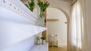A white, rustic interior with a wooden bench, two small potted plants, a white chair, and a white shelf with decorative items. - Badia del Casale (Ugento)