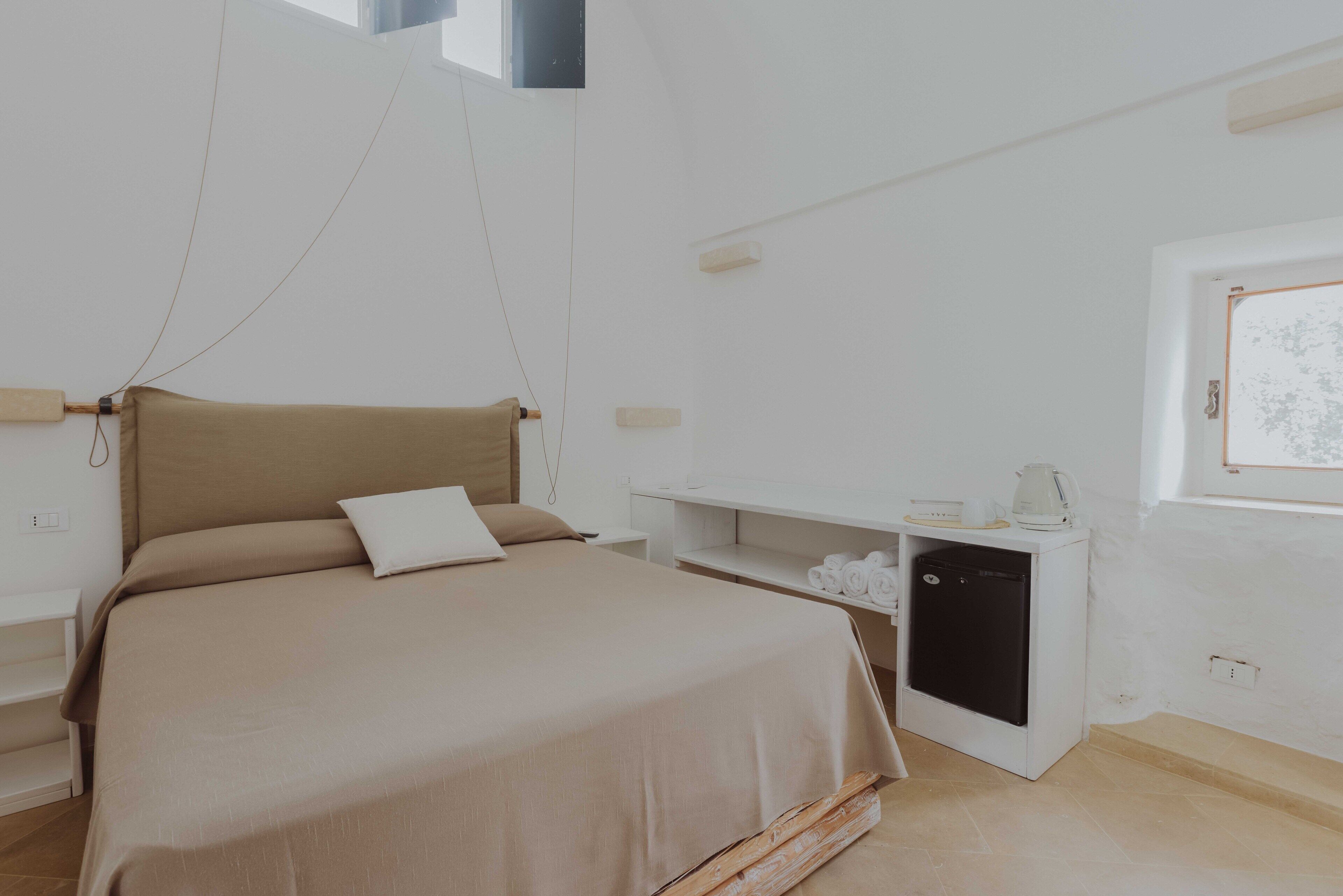 Un dormitorio moderno con cama, mesitas de noche, un armario pequeño blanco y una ventana.