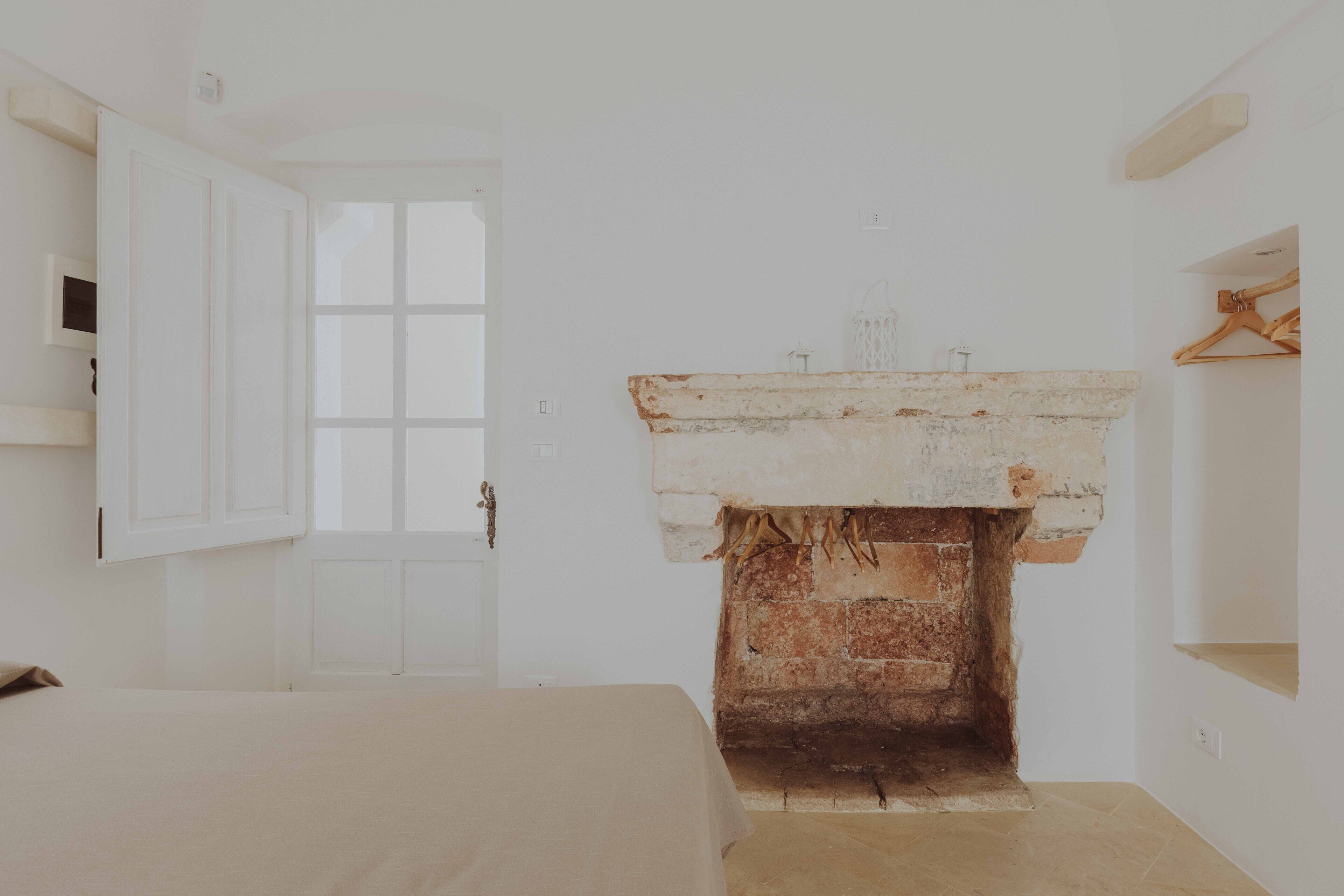 Una habitación con una puerta blanca, chimenea de ladrillo y una cama.