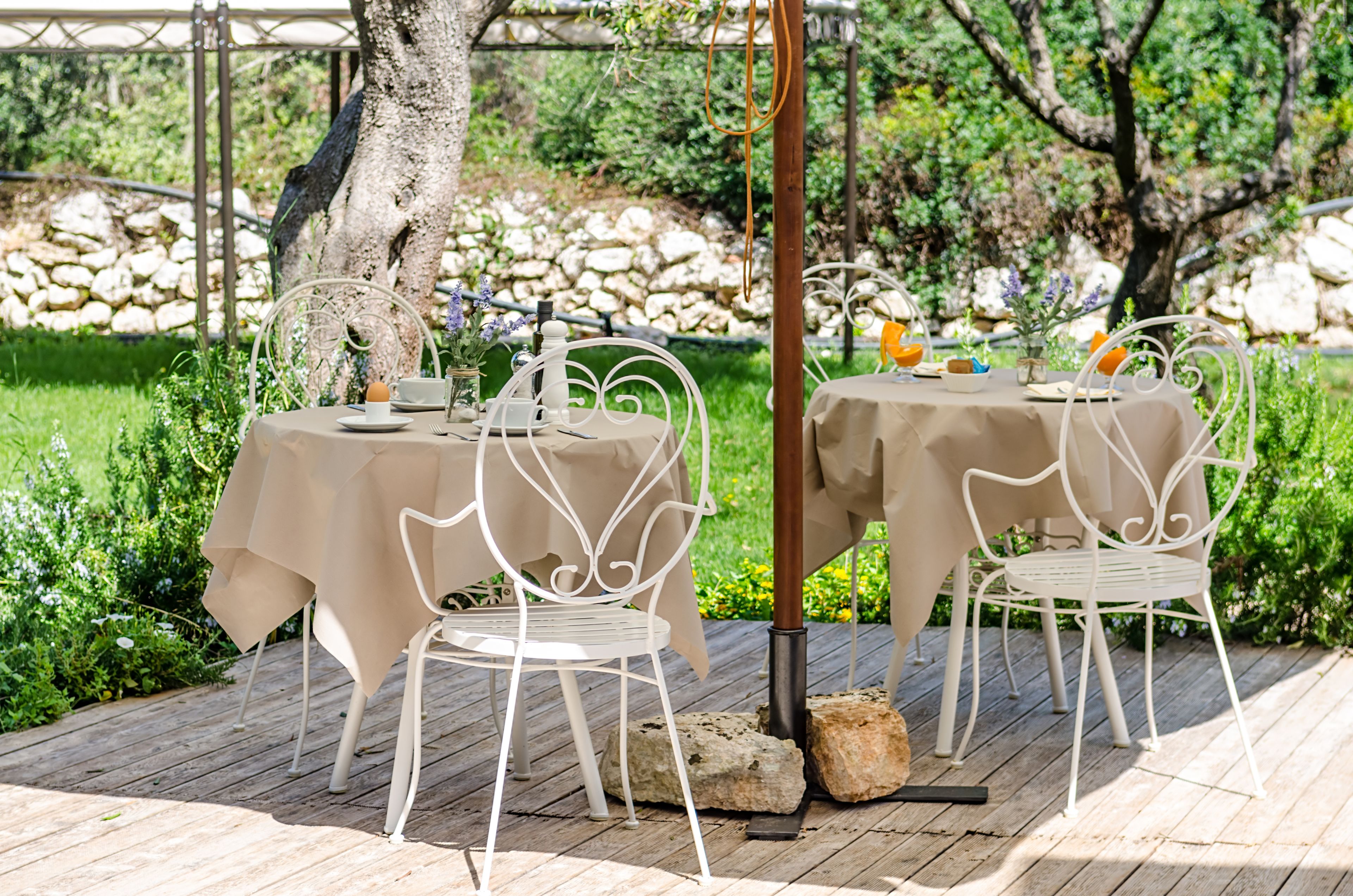 An outdoor dining area with two tables, white metal chairs, and a stone wall in the background.