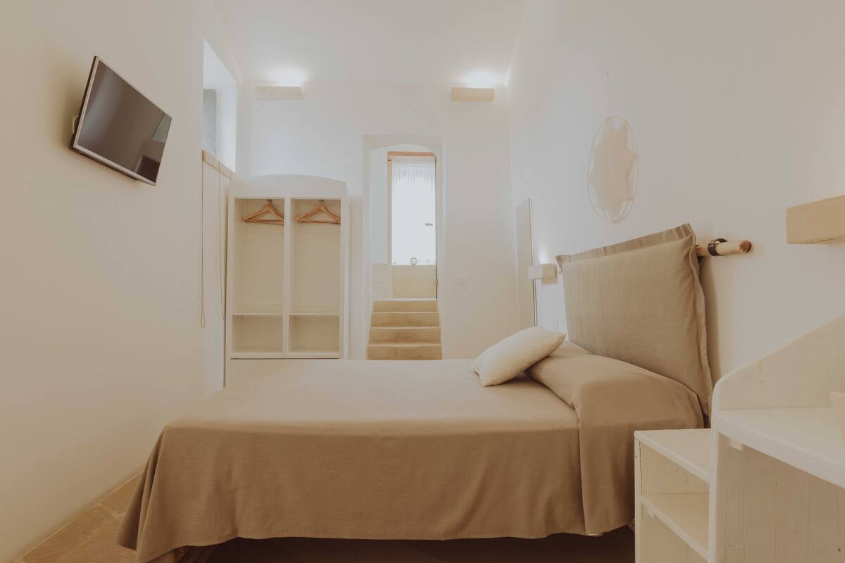 Quarto com cama, televisão, guarda-roupa e escadas.