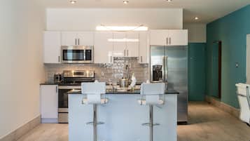 A modern kitchen with white cabinetry, stainless steel appliances, and a central island with bar stools.