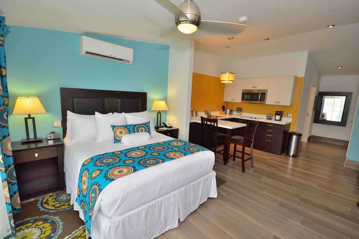 A hotel room with a bed, bedside tables, a desk, and a kitchenette.