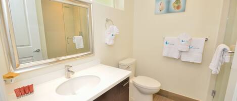 A bathroom with a large mirror, a sink, a toilet, and a shower. There are towels hanging on the wall and a framed picture above the toilet.