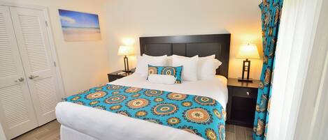 Une chambre d’hôtel bien aménagée, avec un lit, deux tables de chevet, un ventilateur de plafond et une vue sur l’océan.