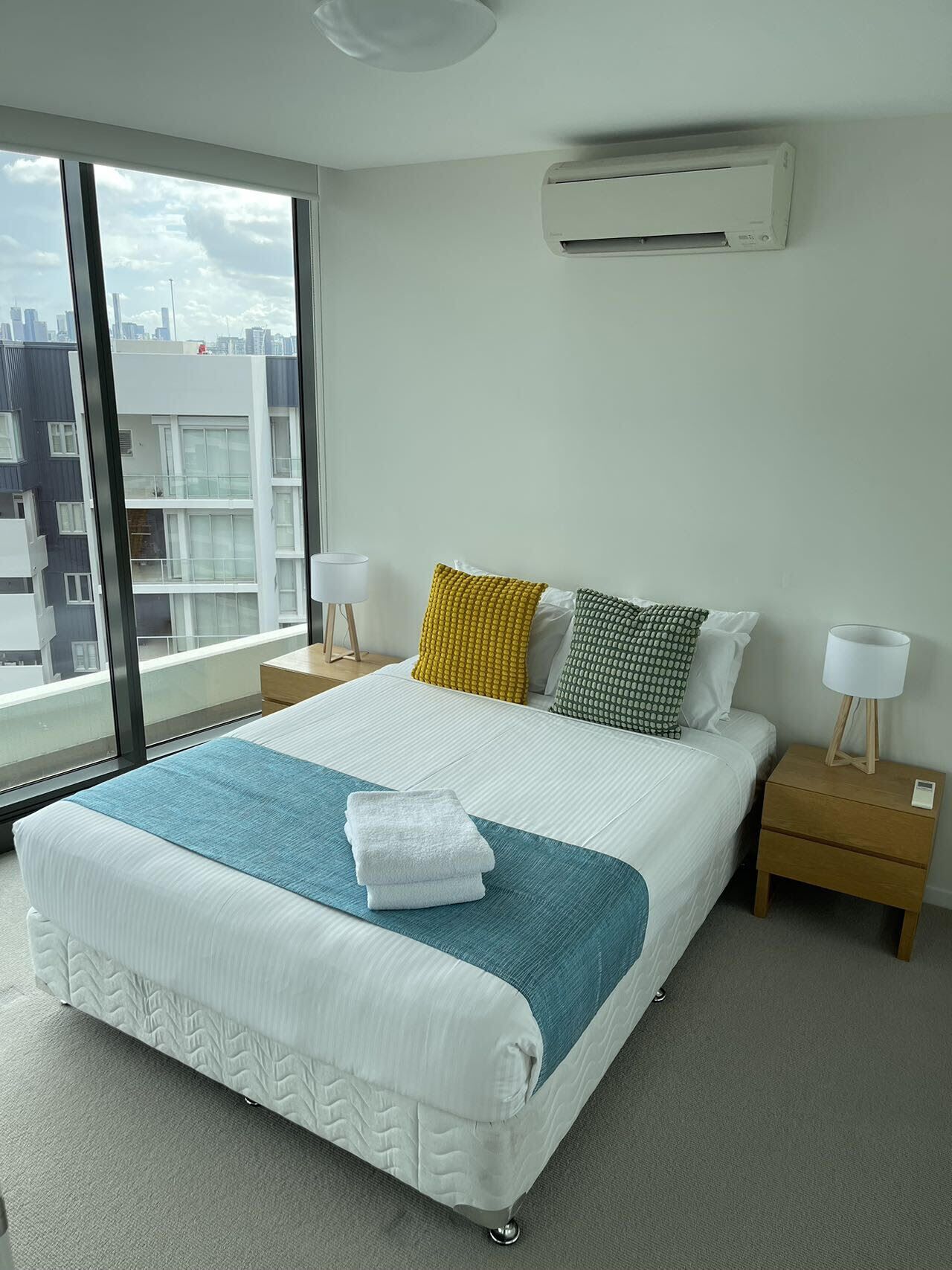 Et moderne hotelværelse med en stor seng, to sengeborde, et vindue med udsigt over byen og en aircondition på væggen.