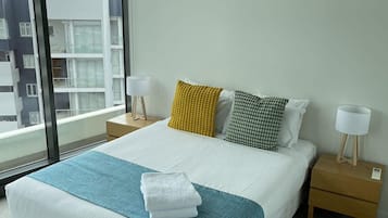 A modern hotel room with a large bed, two bedside tables, a window with a city view, and an air conditioning unit on the wall.