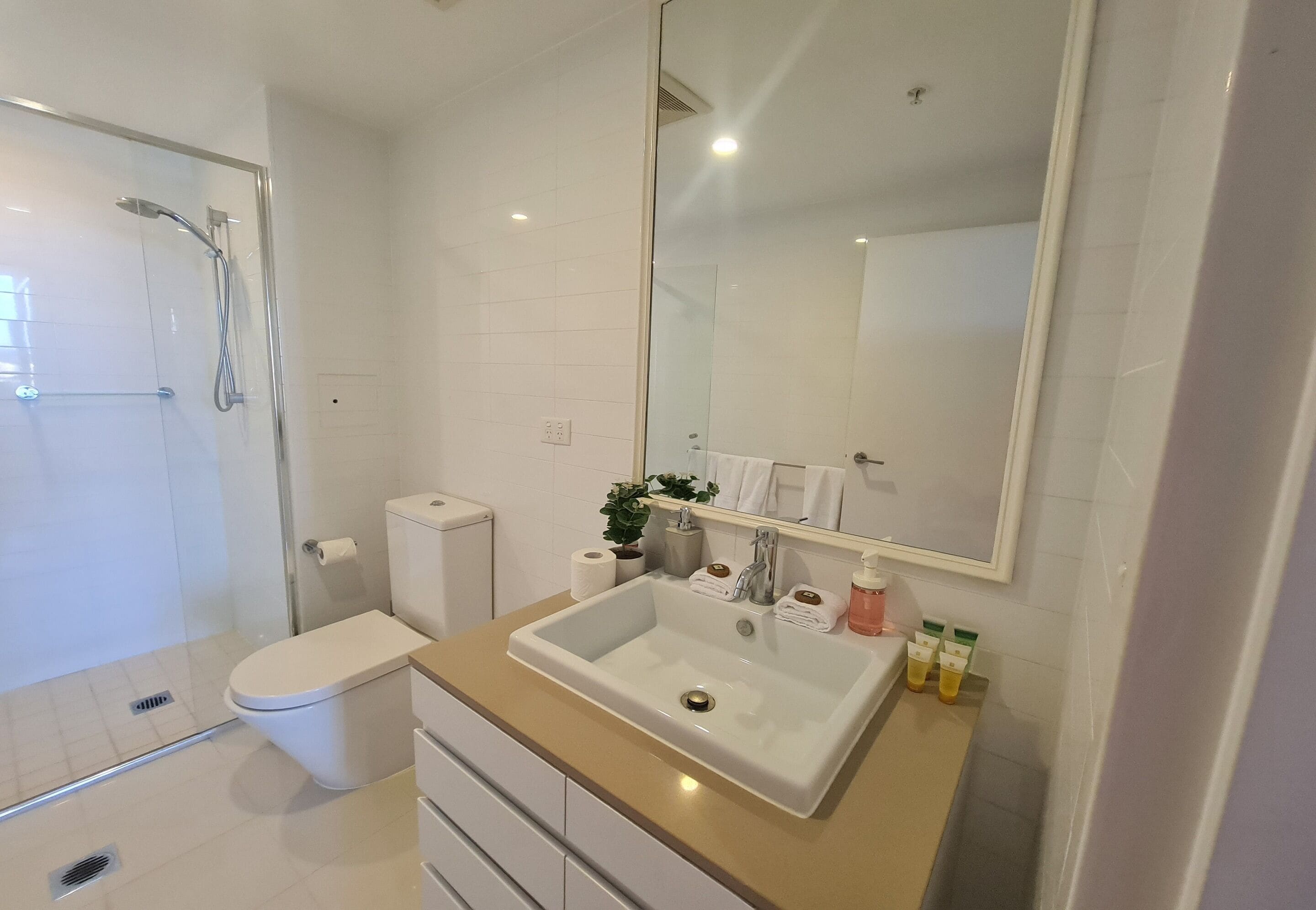 Un bagno moderno con cabina doccia in vetro, un water bianco, un mobile lavabo color beige e uno specchio grande.