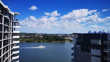 Un bâtiment moderne doté de balcons donnant sur une étendue d’eau, avec un yacht sur l’eau et une vue sur la ville au loin.