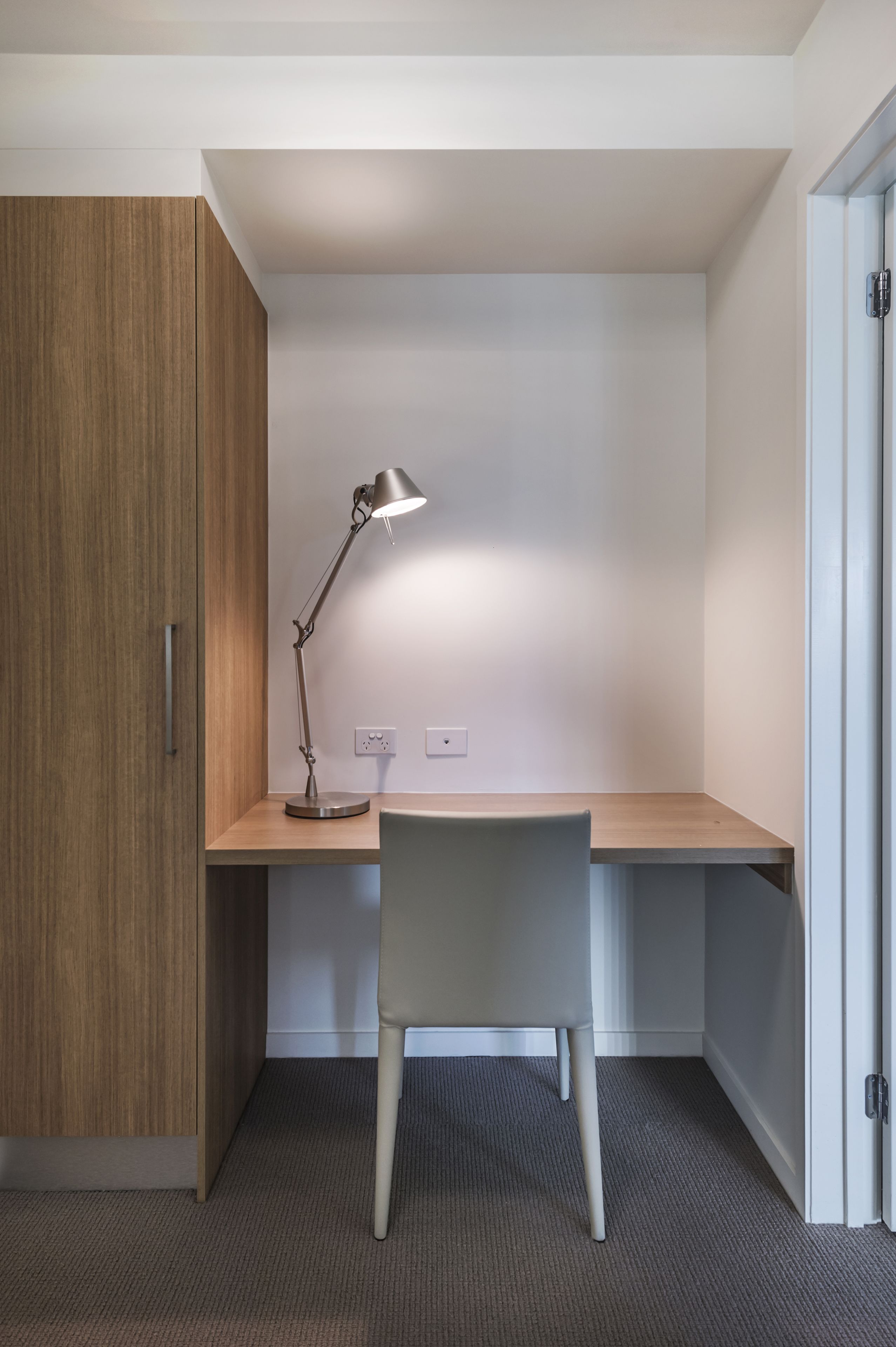 Un espacio de trabajo pequeño y bien iluminado, con escritorio, silla y lámpara de escritorio.