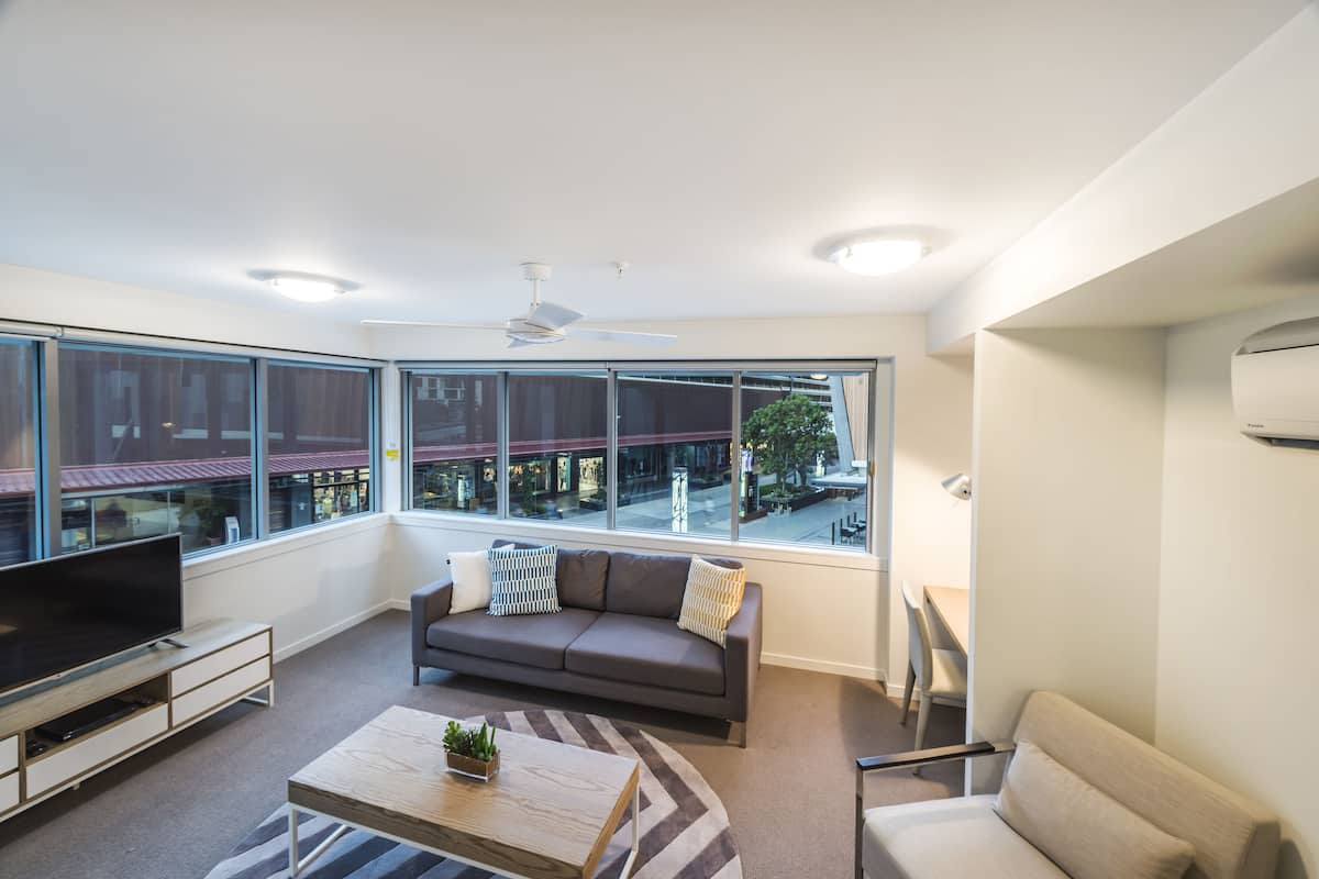 A modern living room with a large window, a sofa, a coffee table, and a TV.