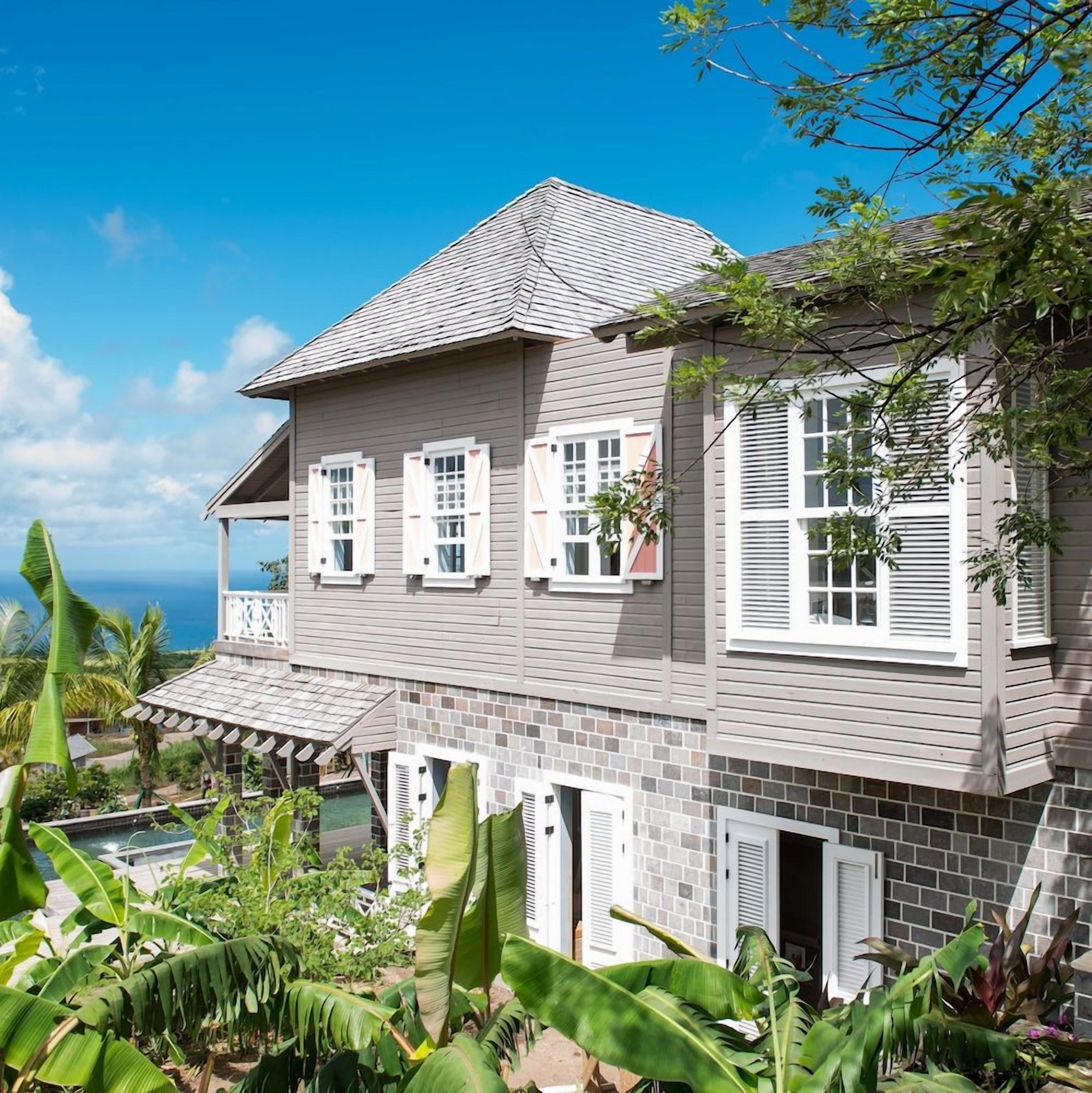 A two-story building with a balcony, a pool, and lush tropical vegetation.