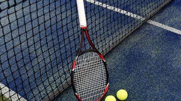 A tennis court with a net, a tennis racket, and three tennis balls.