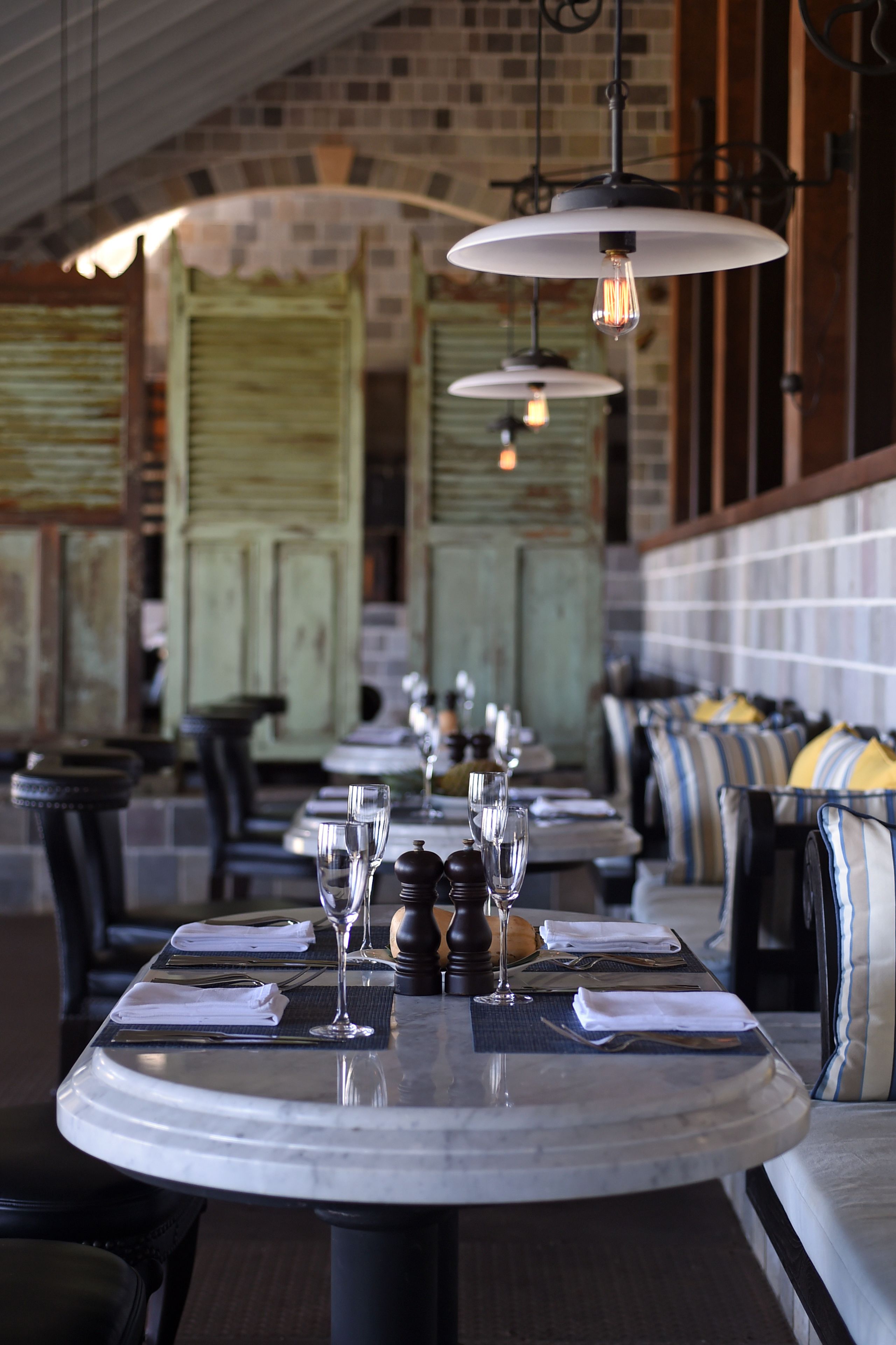 A restaurant with round tables set for dining, featuring a brick wall and wooden furniture.