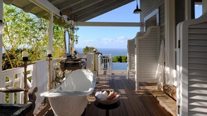 Une terrasse en bois avec une baignoire blanche, une petite table et une vue sur l’océan.