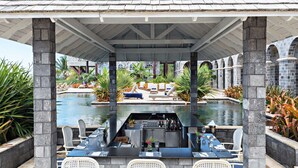 Un espace extérieur avec piscine, des chaises longues, un bar et un coin salon couvert offrant une vue sur la piscine.
