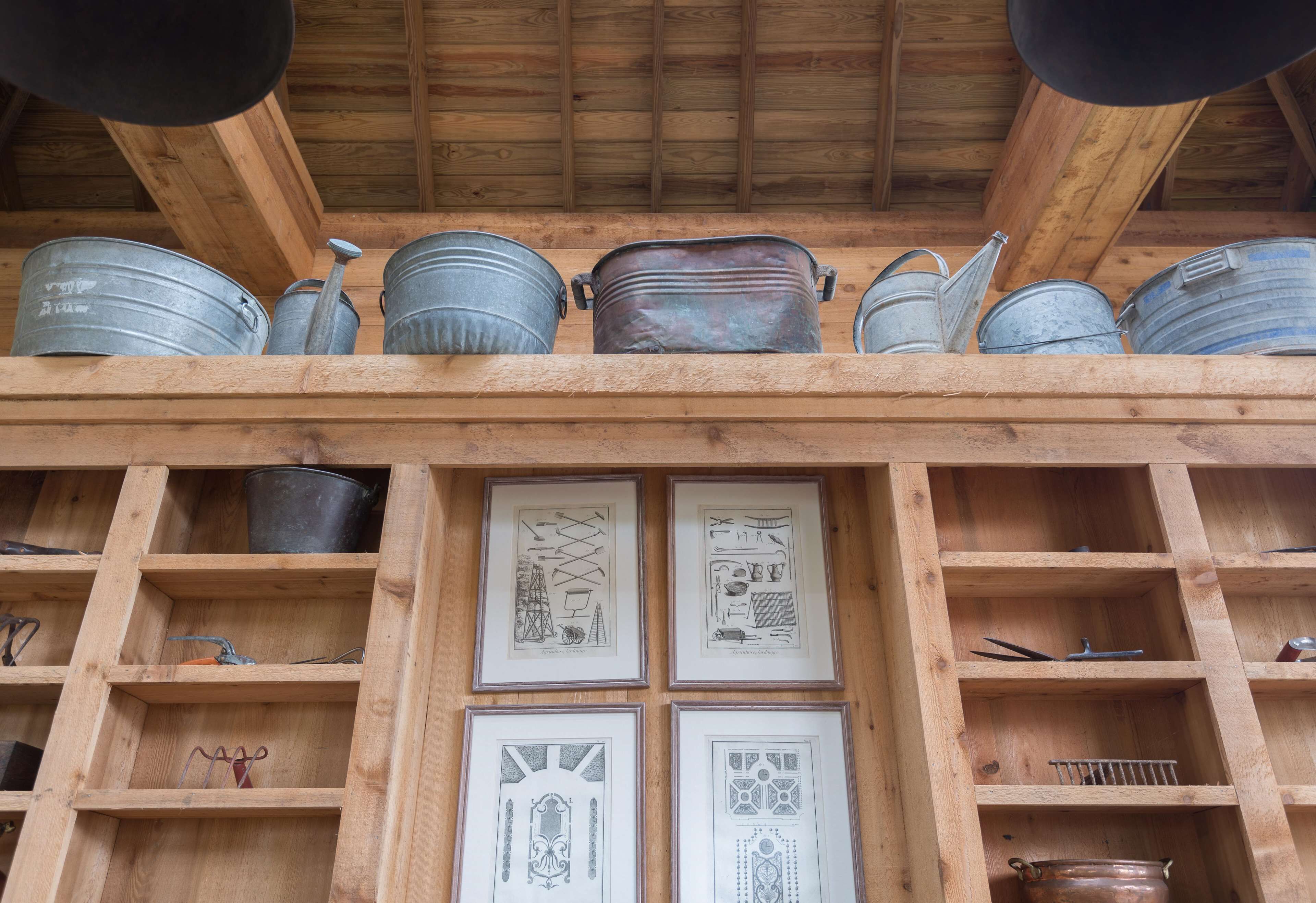 A wooden ceiling with metal buckets and pots, and framed architectural drawings on the walls.
