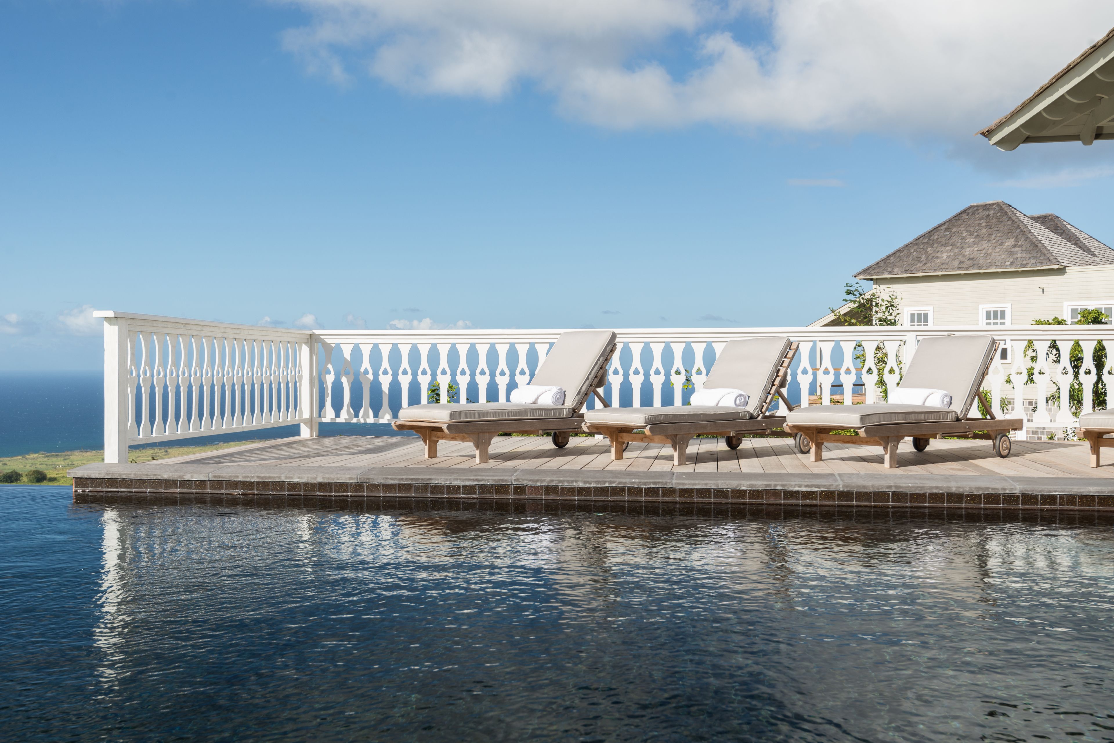 A poolside area with lounge chairs and a white fence overlooking a body of water.