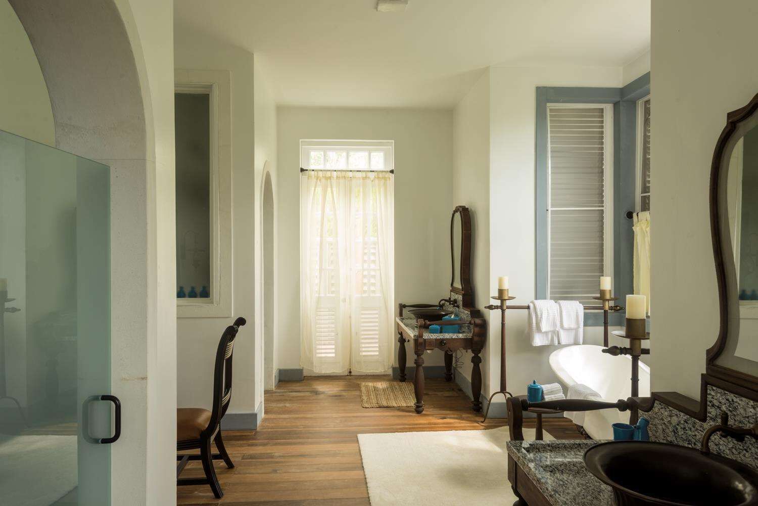 A bathroom with a wooden floor, a sink, a mirror, and a window with curtains.