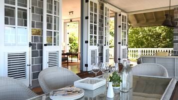 A covered patio with wicker furniture, a glass table, and a view of the garden.