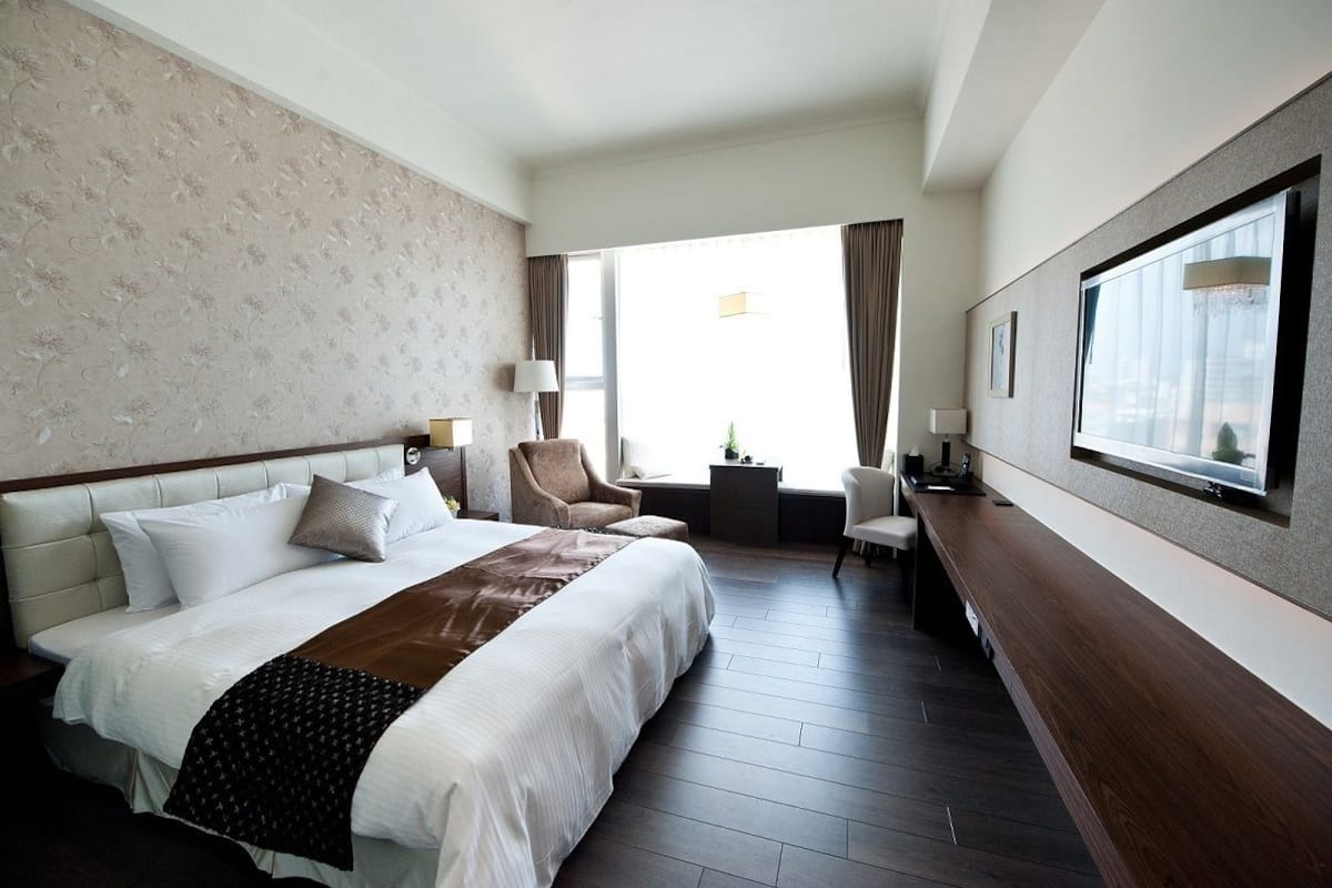 A hotel room with a large bed, a desk, a chair, and a view of the city.