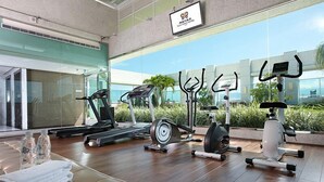 A modern gym with various exercise equipment, a large window, and a sign indicating the gym's name. - Yuh Tong Hotel (Chiayi City)