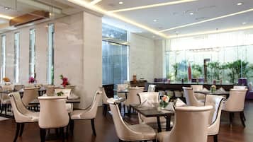 A modern dining area with multiple tables and chairs, large windows, and indoor plants.