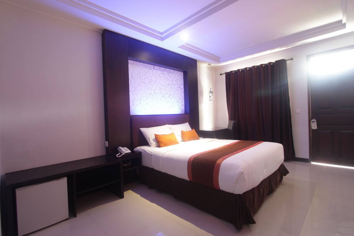 A modern hotel room with a large bed, a bedside table with a phone, and a small cabinet.