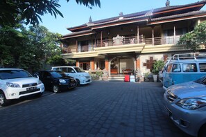 A traditional building with a balcony, parked cars, and a red trash bin. - Taman Agung Hotel (Denpasar)