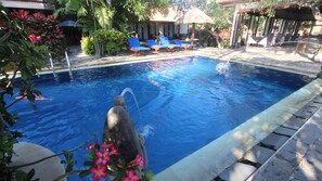 A swimming pool with lounge chairs and a stone structure in the foreground. - Taman Agung Hotel (Denpasar)