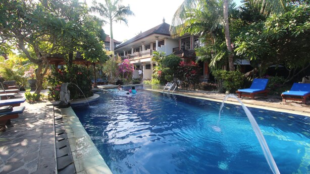 A swimming pool with lounge chairs and a building in the background. - Taman Agung Hotel (Denpasar)