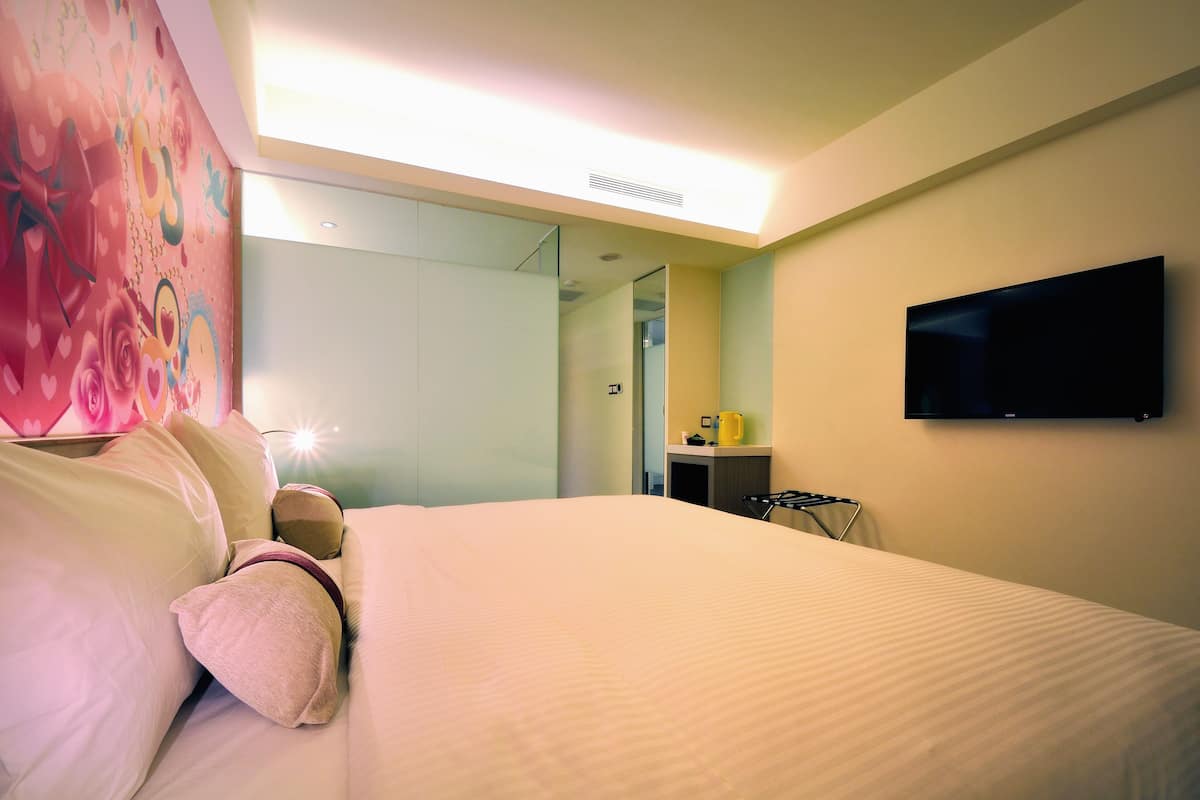 A hotel room with a bed, a flat-screen TV mounted on the wall, and a mirror reflecting the room.