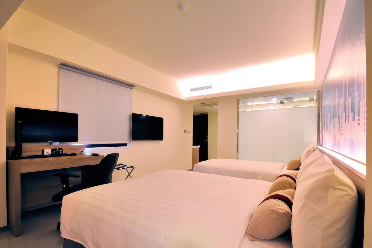 A hotel room with two beds, a desk with a TV, and a window with a cityscape view.