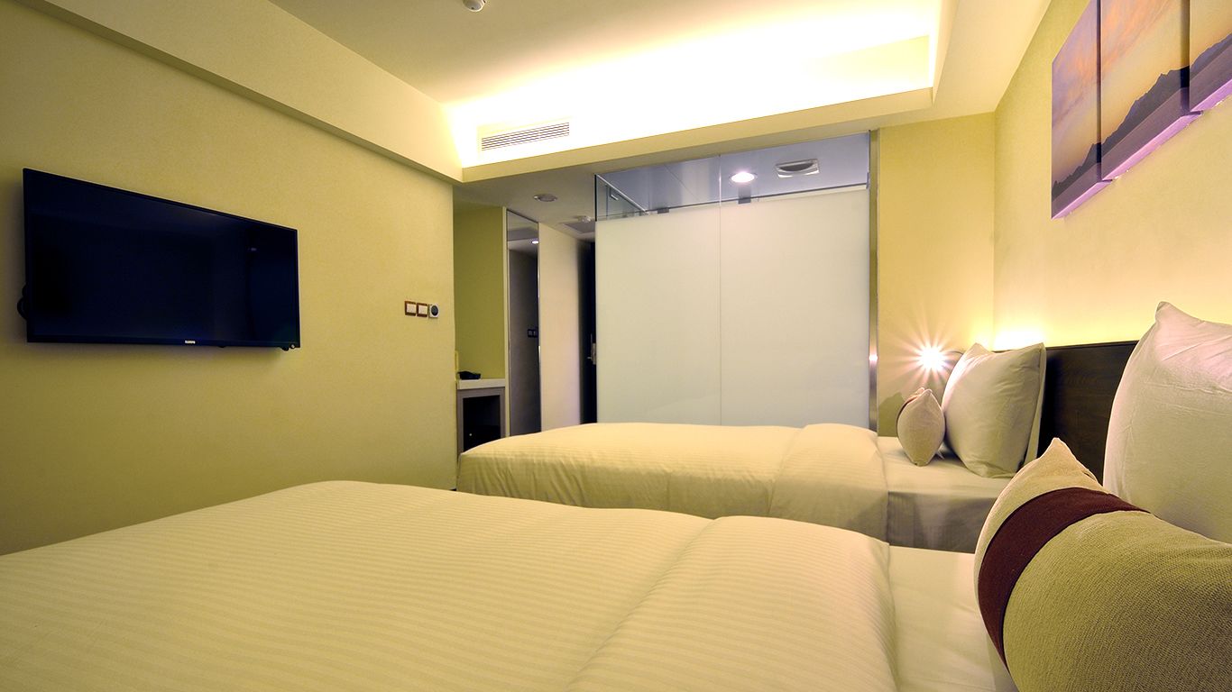 A hotel room with two beds, a flat-screen TV mounted on the wall, and a large mirror reflecting the room.